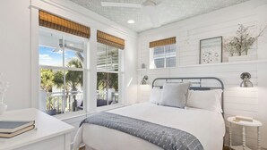 Quarto com uma cama grande, uma escrivaninha e uma janela com vista para palmeiras.