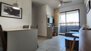 A modern hotel room with a kitchenette, a dining area, a sofa, and a large window with a view.