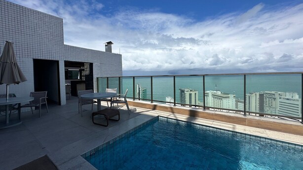 A modern outdoor pool area with a view of the ocean and city skyline.