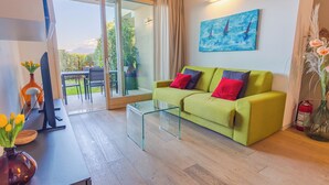Una sala de estar moderna con una mesa de centro de vidrio, un sofá con cojines coloridos, un cuadro en la pared y vistas al exterior.