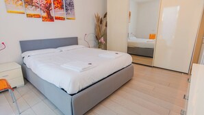 A modern bedroom with a grey bed, white linens, a nightstand, a mirror, and a door leading to another room. - Profumo di Rosa - One Bedroom Apartment, Sleeps 4 (Desenzano del Garda)