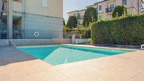 A swimming pool with a lifebuoy, surrounded by a tiled deck, and adjacent to a building with balconies. - Profumo di Rosa - One Bedroom Apartment, Sleeps 4 (Desenzano del Garda)