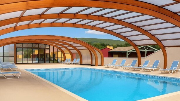 Una piscina interior con techo de cristal, sillas de descanso azules y vistas del paisaje circundante.