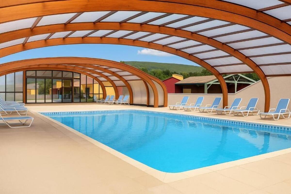 An indoor swimming pool with a glass ceiling, blue lounge chairs, and a view of the surrounding landscape.