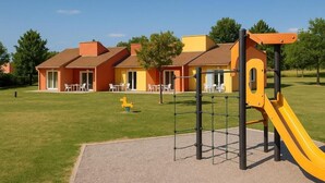 Un parque infantil con un tobogán amarillo y una estructura para escalar, rodeado por un edificio con múltiples ventanas y puertas.