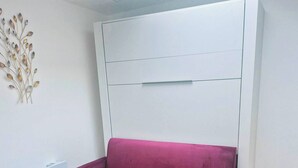 Una stanza con un divano viola, un tappeto decorato, un muro bianco e una lampada a soffitto.
