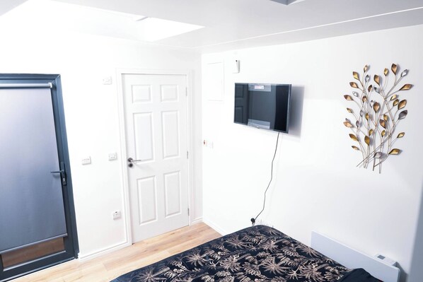 A bedroom with a bed, a TV, a door, and a wall decoration. - A Cozy Studio Apartment (Kilgobbin)