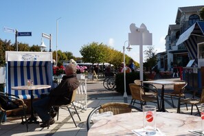 Ein Straßencafé mit Tischen und Stühlen, ein Schild für das Hotel Seestern und ein Wegweiser.