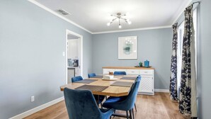 A dining area with a wooden table, blue chairs, a kitchen in the background, and a ceiling light fixture. - NEW 4BR Home Nearby ACU & Downtown - Family Vacation - Summer Savings- Sleeps 10 (Abilene)