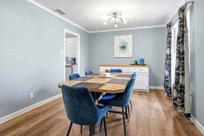 Ein Essbereich mit Holztisch, blauen Stühlen, einer Küche im Hintergrund und einer Deckenleuchte.