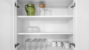 A white cabinet with shelves containing clear glasses, a green vase, and white mugs. - NEW 4BR Home Nearby ACU & Downtown - Family Vacation - Summer Savings- Sleeps 10 (Abilene)