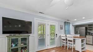 A modern kitchen with a built-in refrigerator, a dining area with white chairs, and a television mounted on a cabinet. - Sonesta III 202 by Seaside Vacations & Sales (Ocean City)