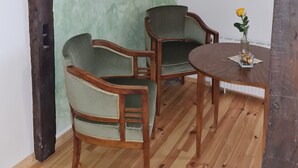 Ein Zimmer mit Holzboden, zwei mit Stoff bezogene grüne Sessel, ein kleiner Holztisch mit einer Vase und einem Bilderrahmen.
