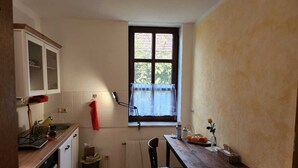 Eine kleine Küche mit Fenster, Heizkörper, Holztablett und Stuhl.