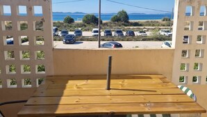 A wooden table and chairs on a balcony with a view of parked cars and the sea.