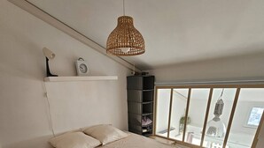 A bedroom with a large bed, a wooden floor, a hanging light fixture, and a window with a view.