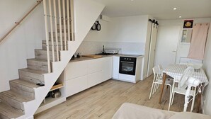 A modern kitchen with a built-in oven, a dining area with a table and chairs, and a staircase with wooden steps.