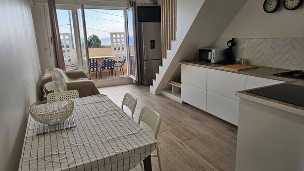 A modern kitchen with a dining area, a view through a glass door, and a staircase leading to an upper level.