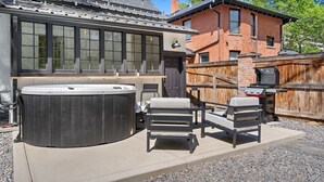 Una vasca idromassaggio, due sedie, un barbecue e un recinto di legno in un giardino.