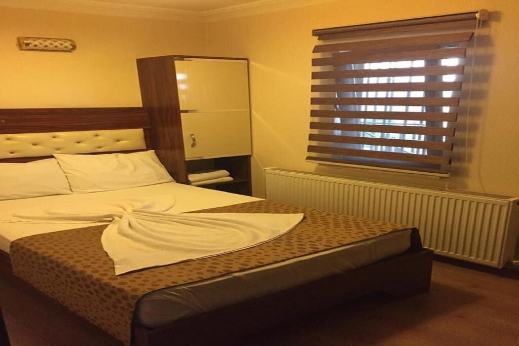 A hotel room with a bed, a wardrobe, a radiator, and a window with blinds.