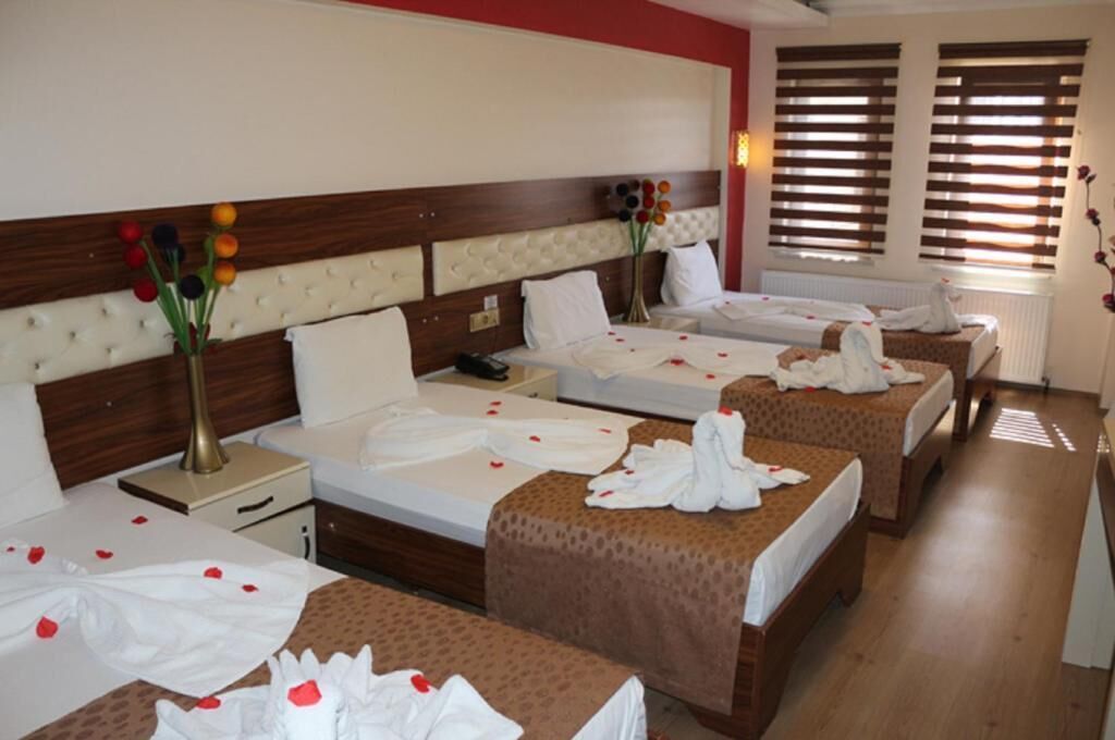 A hotel room with two beds, a wooden headboard, bedside tables, and a window with blinds.
