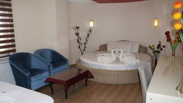 A hotel room with a bed, two blue armchairs, a small table, a vase with flowers, and a wall-mounted light fixture.