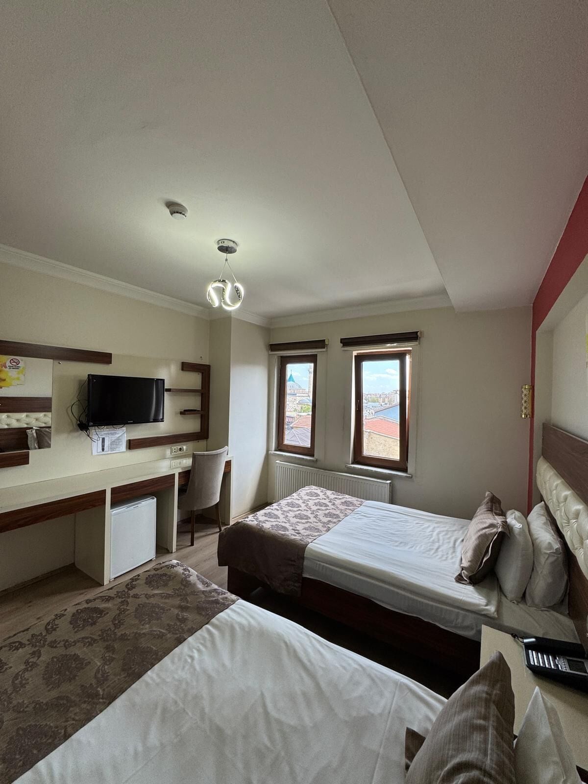 Ein Hotelzimmer mit einem Bett, einem Schreibtisch mit Computer, einem Fernseher und zwei Fenstern.