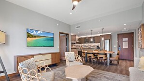 Ein modernes Wohnzimmer mit großem Fernseher, Korbmöbeln, einer Essecke und einer Küche im Hintergrund.