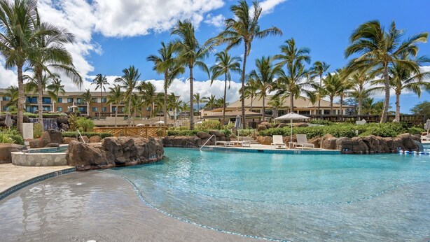 Ein Hotelpool mit Palmen, einem Wasserfall und einer Felsformation.