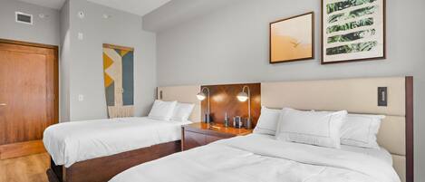 Une chambre d’hôtel avec deux lits, une armoire en bois, un ventilateur de plafond et deux œuvres d’art encadrées accrochées au mur.