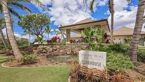Schild für 'Maui Bay Villas Clubhouse' mit einem angelegten Garten, der Palmen, einen kleinen Teich und ein Gartenhaus zeigt.