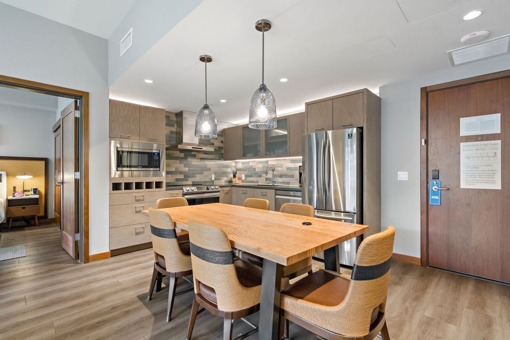 A modern kitchen with stainless steel appliances, a wooden dining table, and woven chairs.