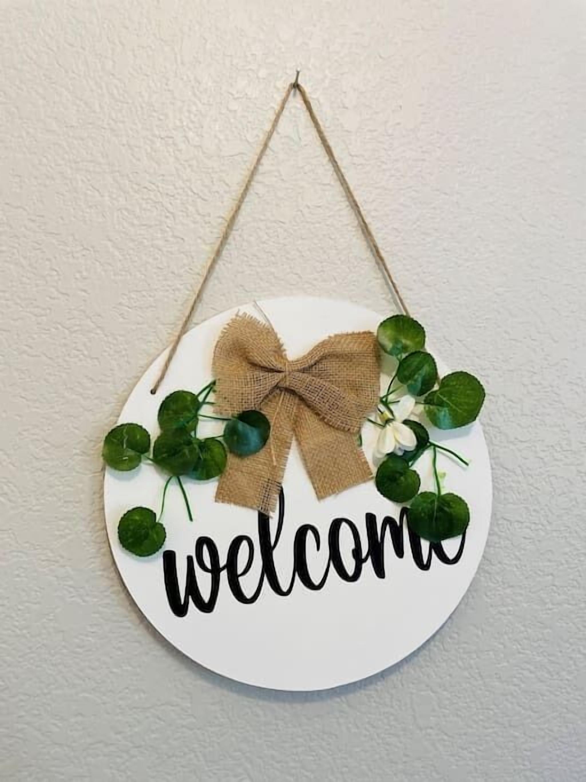 A circular welcome sign with a burlap bow and greenery.