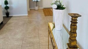 A hallway with a white wall, a gold-framed console table, a potted plant, and a door in the background. - Comfy-cozy 1BR home in gated 55+ community (Goodyear)