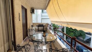 A balcony with a glass table and chairs, a view of the street, and a yellow awning.