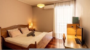 A bedroom with a wooden bed, a desk with a chair, a lamp, and a window with curtains. - Cozy Apartment in Faliro (Paleo Faliro)