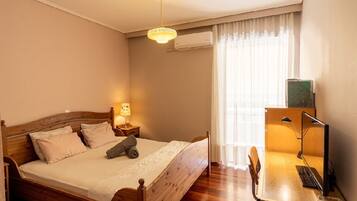 A bedroom with a wooden bed, a desk with a chair, a lamp, and a window with curtains.
