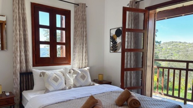 A bedroom with a bed, a window, a door, and a view of the outdoors. - St Visianos stone house (Filousa)