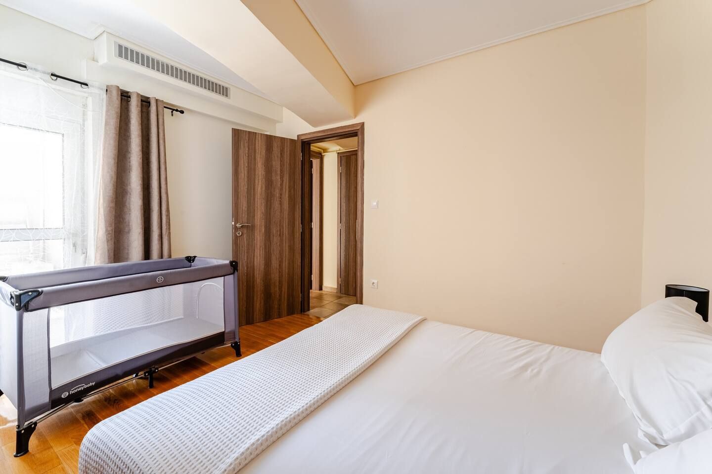Une chambre d’hôtel avec un lit, un berceau, une porte et une fenêtre avec des rideaux.
