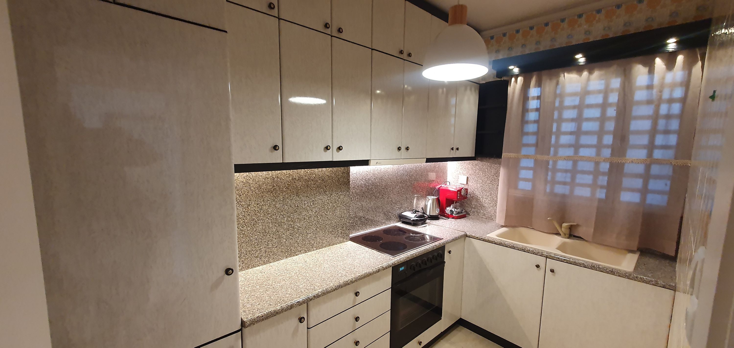 A kitchen with white cabinets, a granite countertop, a coffee machine, and a window with a grid pattern.