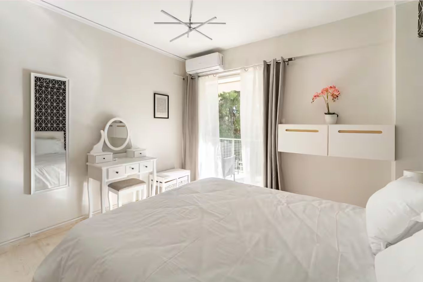 Een slaapkamer met een bed, een dressoir, een spiegel en een raam met gordijnen.