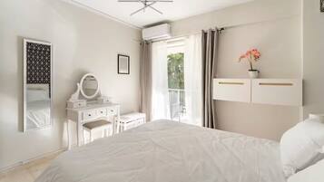 Een slaapkamer met een bed, een dressoir, een spiegel en een raam met gordijnen.
