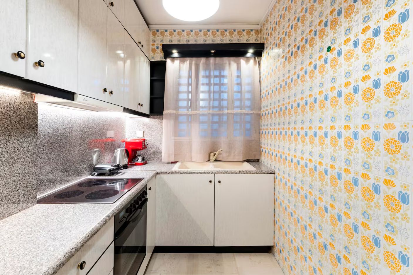 A compact kitchen with a stove, sink, and a red coffee machine.