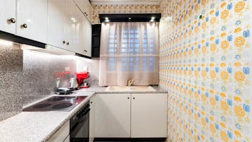 A compact kitchen with a stove, sink, and a red coffee machine.
