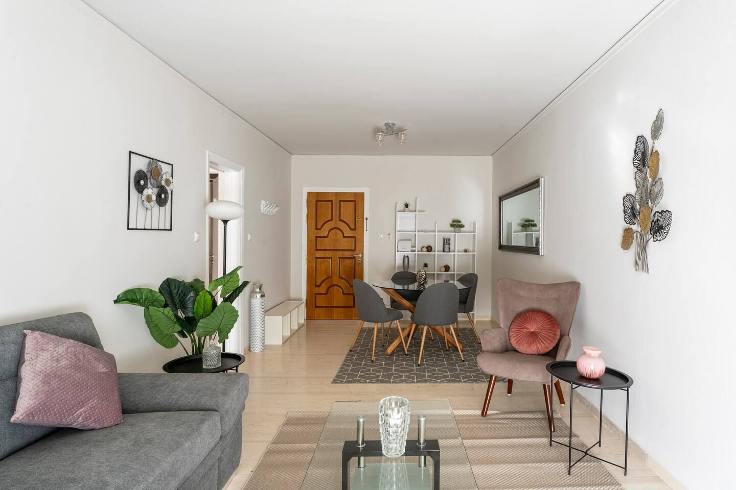 Un salon moderne avec un canapé gris, un fauteuil rose, un coin repas avec une porte en bois et une étagère blanche.