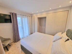 A modern hotel room with a large bed, a television mounted on the wall, and a seating area with a chair. - Seaside 2 level Maisonette 130sqm , 15' Macynia (Macynia)