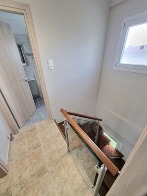 A staircase with a glass railing and wooden handrail, leading to a room with a window.