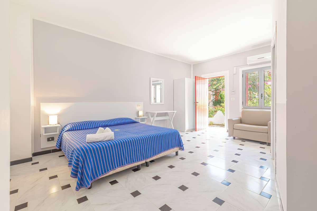 A hotel room with a bed, bedside table, a desk, a chair, and a sofa.