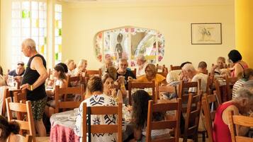 A dining area with wooden chairs and tables, a large mirror, and a yellow wall.