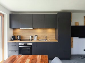 A modern kitchen with dark cabinets, a wooden countertop, a built-in oven, and a sink. - SiLENA Family Apartment (Lajen)
